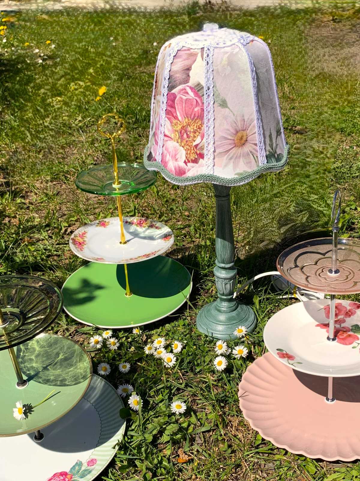 Lampka w stylu vintage z kwiatowym abażurem stojąca na trawie w otoczeniu ręcznie stworzonych ozdobnych pater