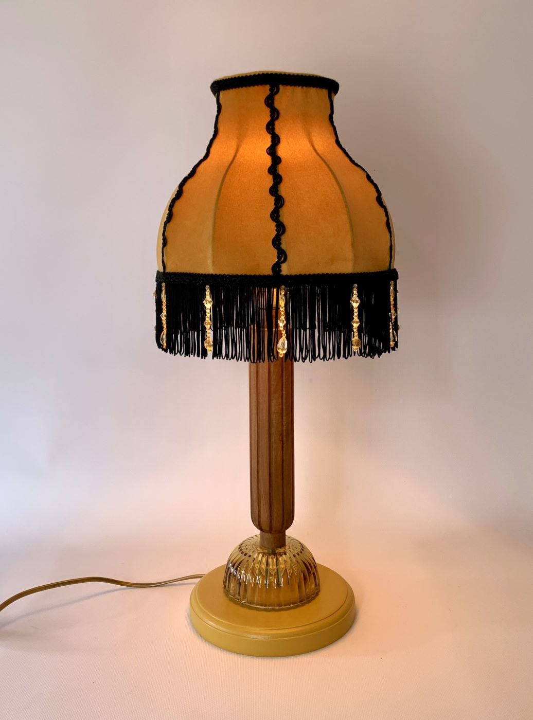 Stojąca lampa z drewnianą podstawą i miodowym abażurem z czarnymi frędzlami.
