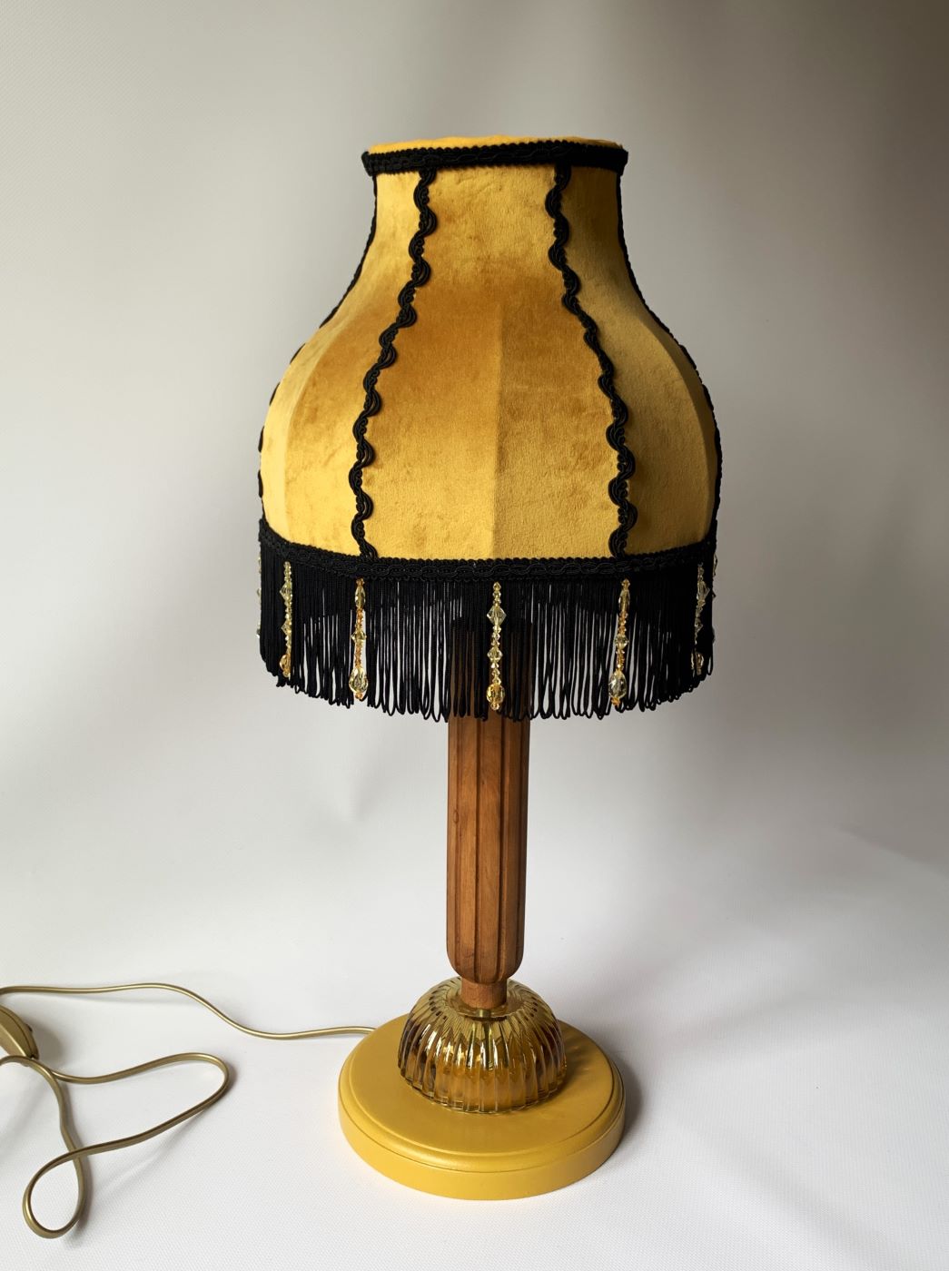 Stojąca lampa z drewnianą podstawą i miodowym abażurem z czarnymi frędzlami.