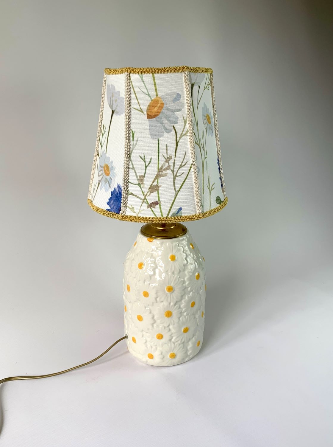 Stojąca lampa z podstawą w kształcie wazonu w biało-żółte stokrotki i z abażurem w rumianki.