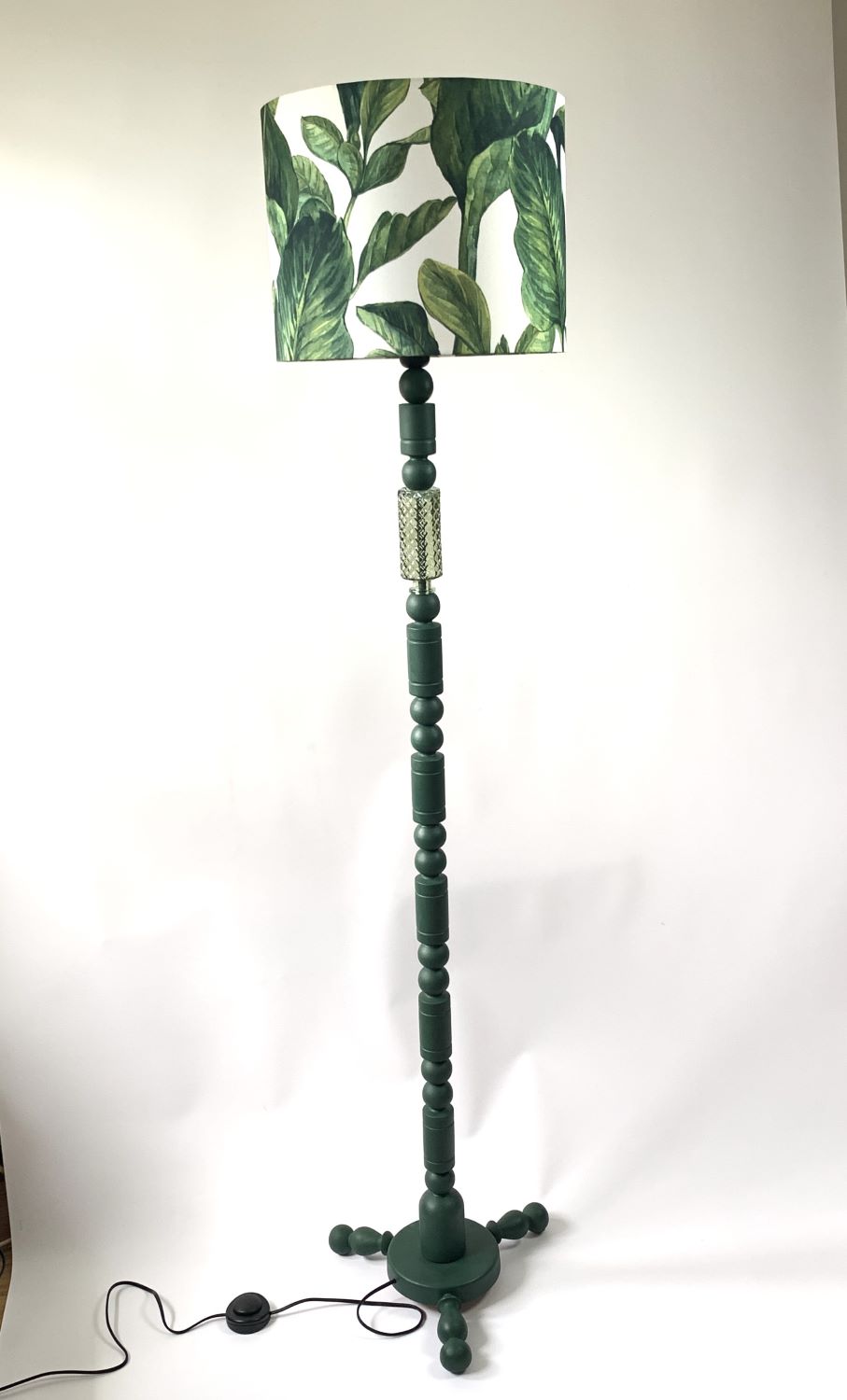 Wysoka lampa podłogowa w kolorze zielonym z abażurem w kształcie walca w duże zielone liście.